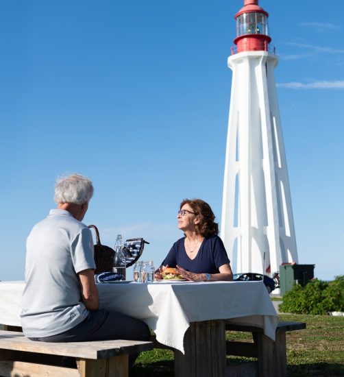 Phare de Pointe-au-Père avec des personnes à une table Site historique maritime de la Pointe-au-Père Crédit SHMP – Lieu historique national du Phare-de-Pointe-au-Père